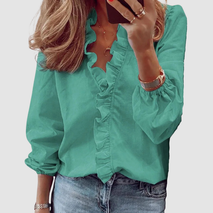 Turquoise blouse with ruffled neckline, worn with jeans in studio setting.