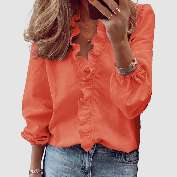 Bright orange blouse with ruffled neckline, paired with jeans in studio setting.
