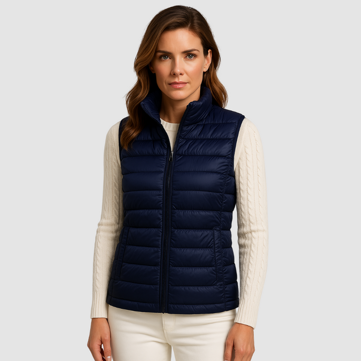 Navy blue puffer vest worn by a woman over a white sweater, studio setting with neutral background.