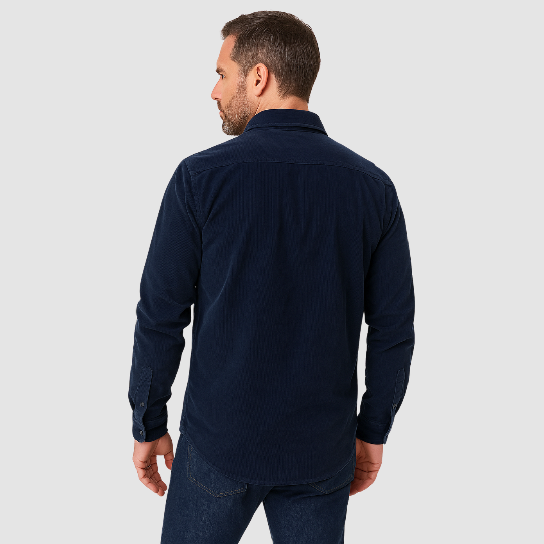 Rear view of a man wearing a navy blue corduroy shirt and jeans, standing against a plain light gray background.