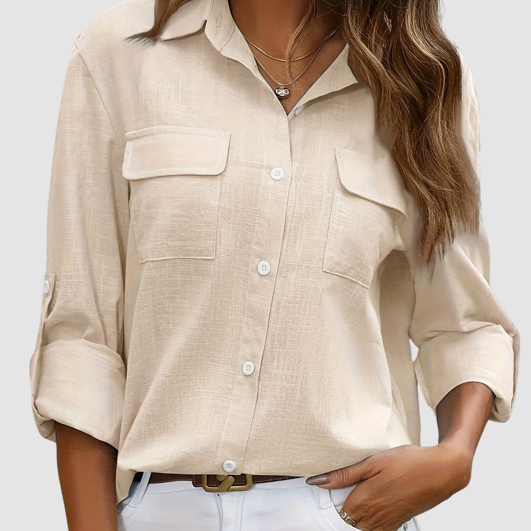 Beige pocket blouse with rolled sleeves, two front pockets, worn with necklaces, studio setting.