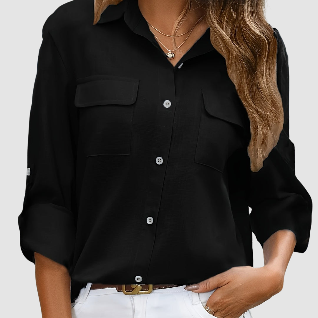 Black pocket blouse with rolled sleeves, two front pockets, worn with necklaces, studio setting.