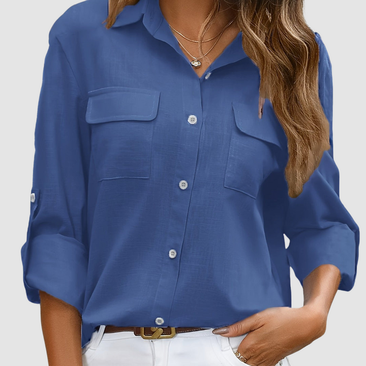 Deep blue pocket blouse with rolled sleeves, two front pockets, worn with necklaces, studio setting.