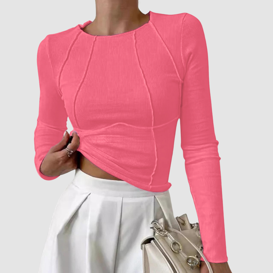 Bright pink long-sleeve top with curved seam details, styled with a white skirt and beige handbag, on a plain white background.