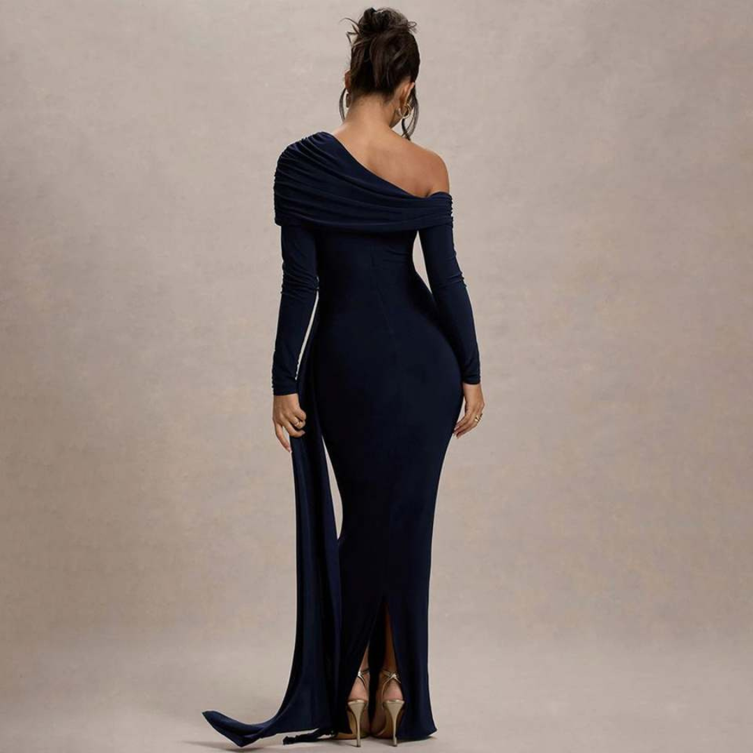 Back view of model in navy off-shoulder maxi dress with draping, standing in studio setting.