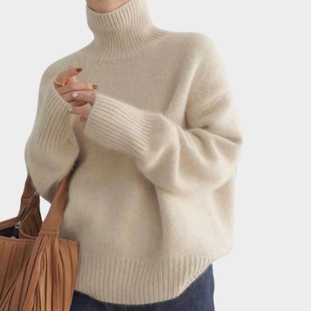 Beige soft turtleneck jumper with long sleeves, paired with blue jeans and brown bag, studio background.