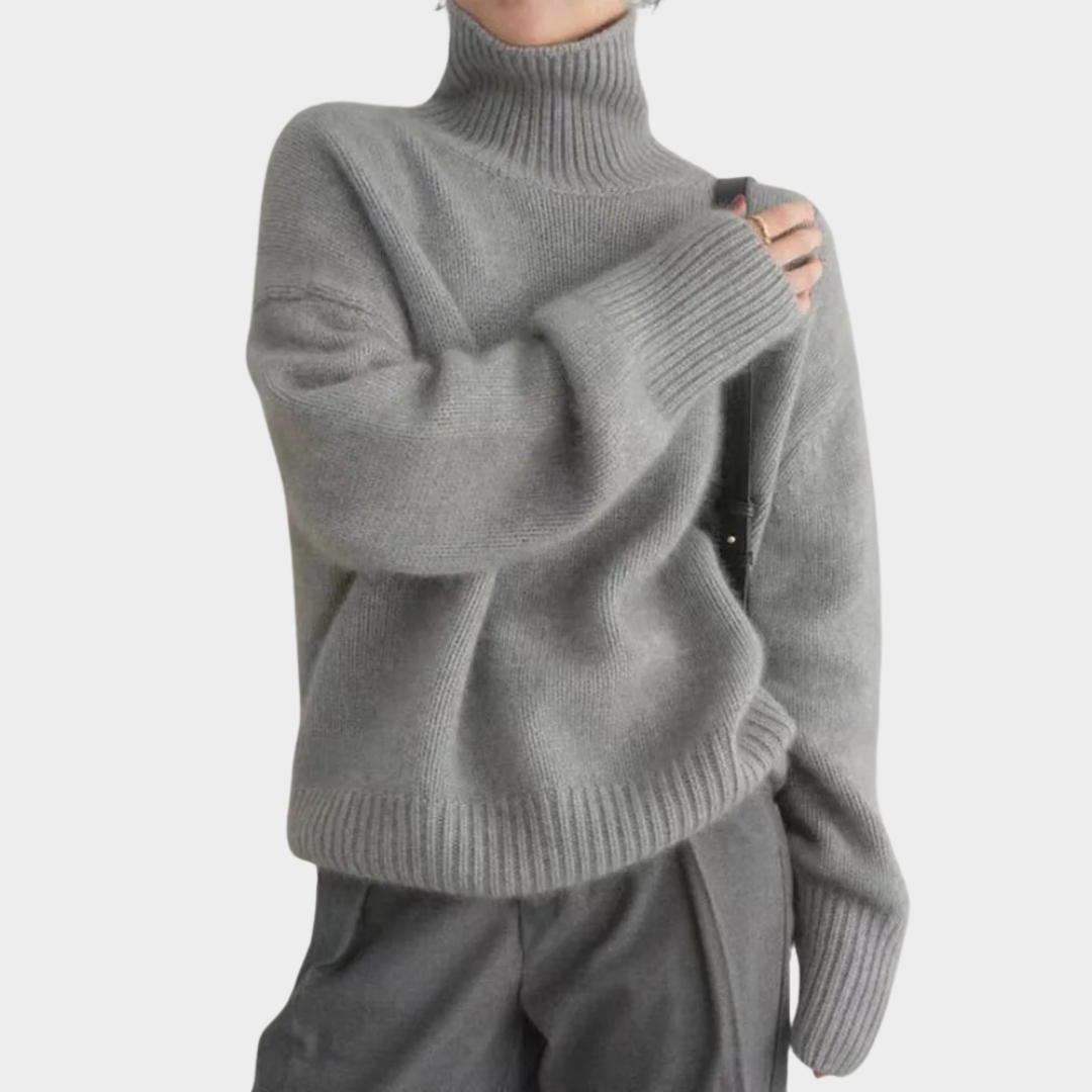 Gray soft turtleneck jumper with ribbed hem and cuffs worn by a model in gray pants, studio background.