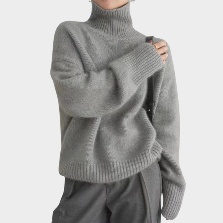 Gray soft turtleneck jumper with ribbed hem and cuffs worn by a model in gray pants, studio background.