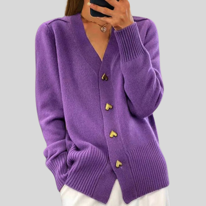 Vibrant purple cardigan with heart-shaped buttons, worn with white pants on a gray background.