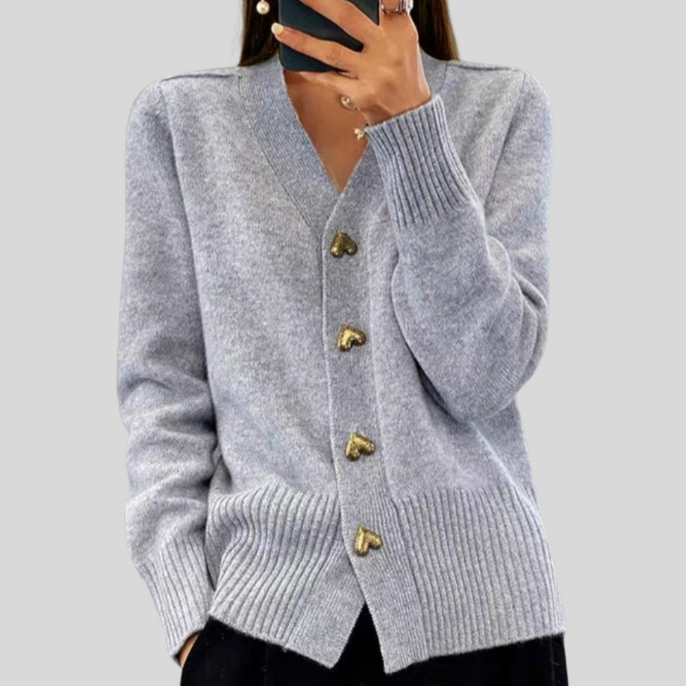 Light gray cardigan featuring heart-shaped buttons, styled with black pants on a gray backdrop.