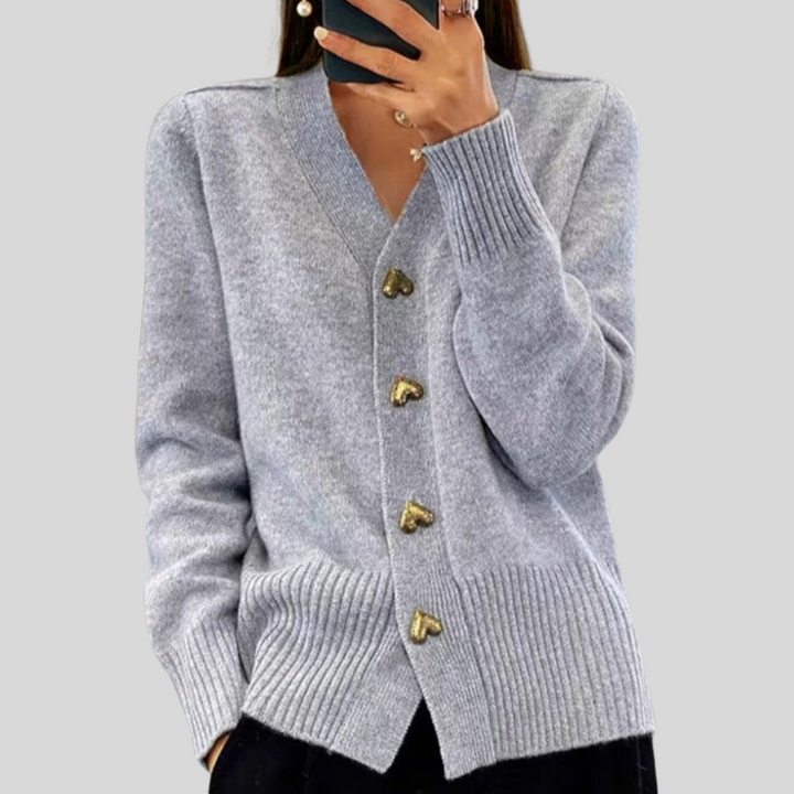 Light gray cardigan featuring heart-shaped buttons, styled with black pants on a gray backdrop.