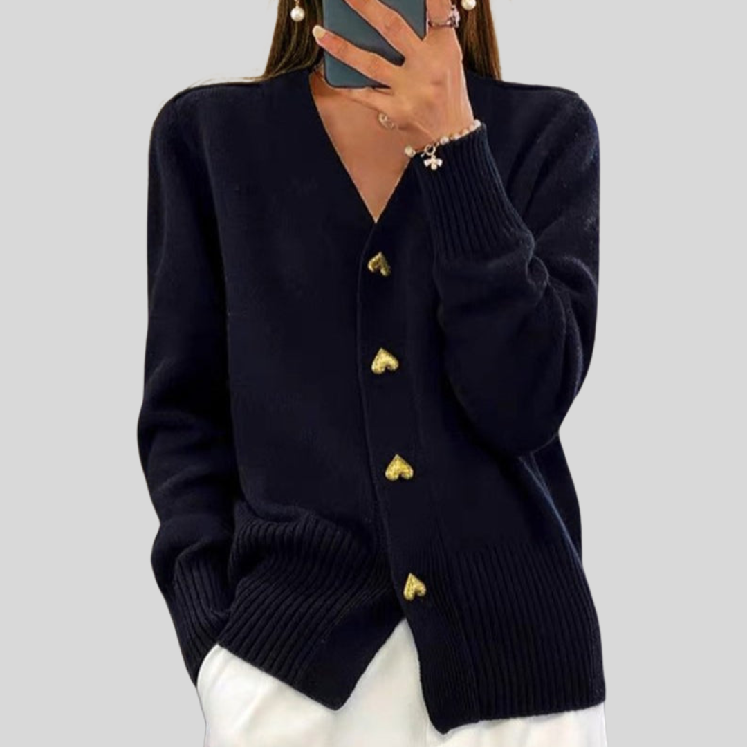 Classic black cardigan with heart-shaped buttons, styled with white pants on a gray backdrop.