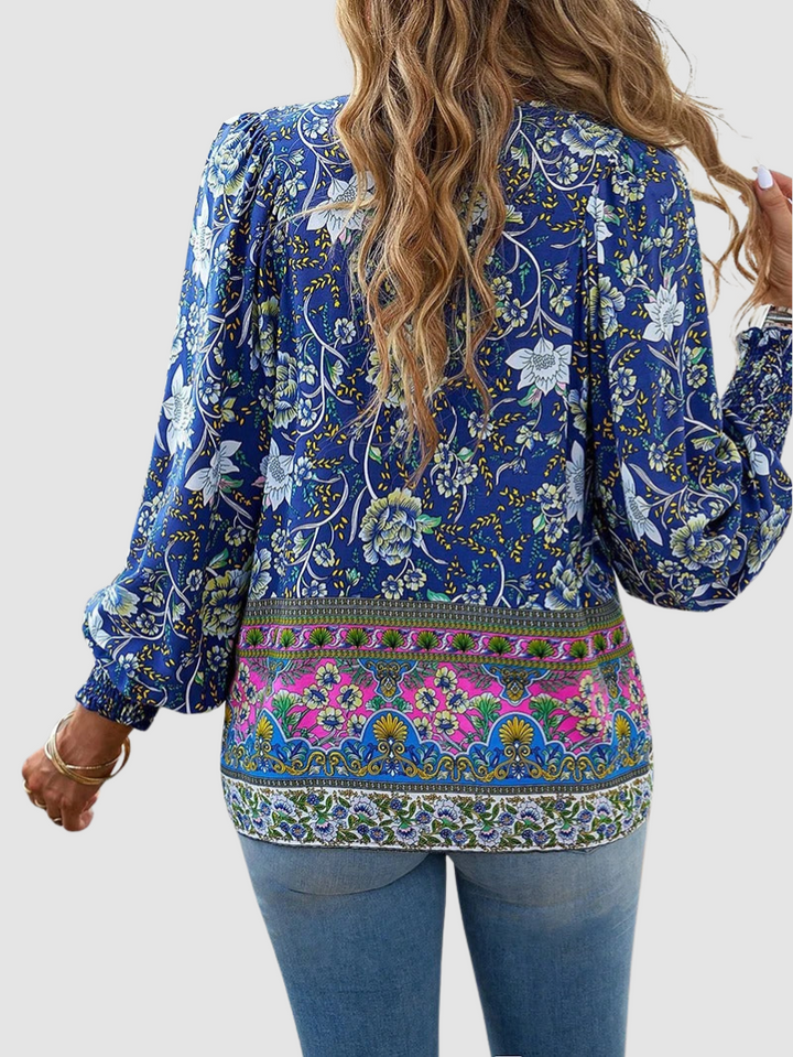 Back view of blue floral blouse with detailed designs, worn with jeans, in a studio setting with neutral background.
