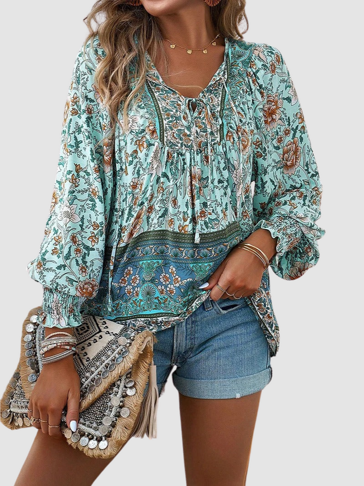 Front view of green floral blouse with detailed designs, paired with denim shorts and textured clutch, on neutral background.