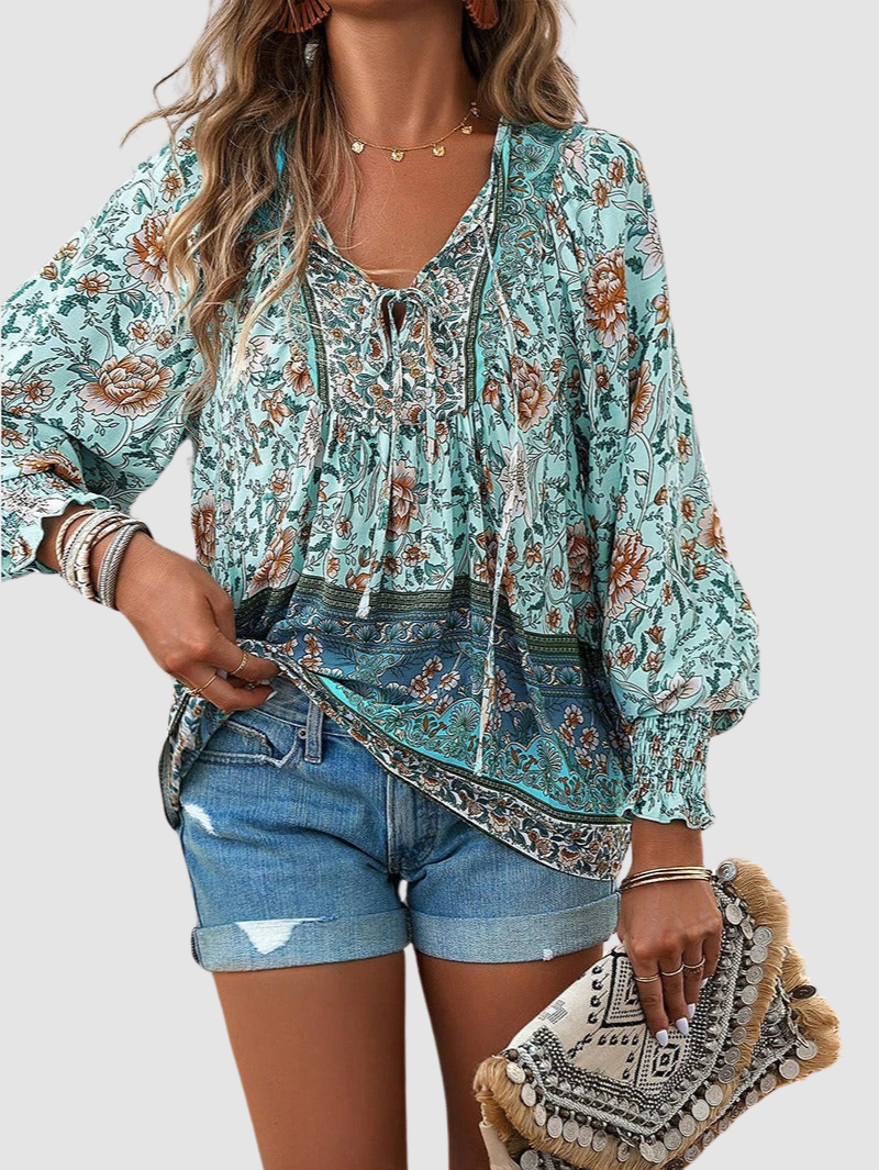 Mint green floral blouse with intricate patterns, styled with denim shorts and a decorative clutch, on gray backdrop.