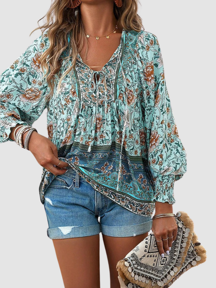 Mint green floral blouse with intricate patterns, styled with denim shorts and a decorative clutch, on gray backdrop.