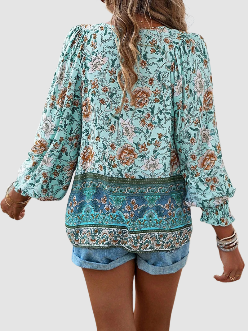 Back view of green floral blouse with ornate patterns, worn with denim shorts, against a gray studio backdrop.