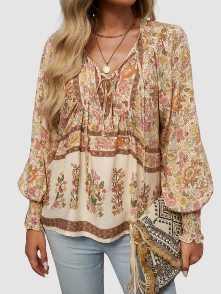 Neutral floral blouse with intricate patterns, paired with light jeans and a textured clutch, on a gray studio backdrop.