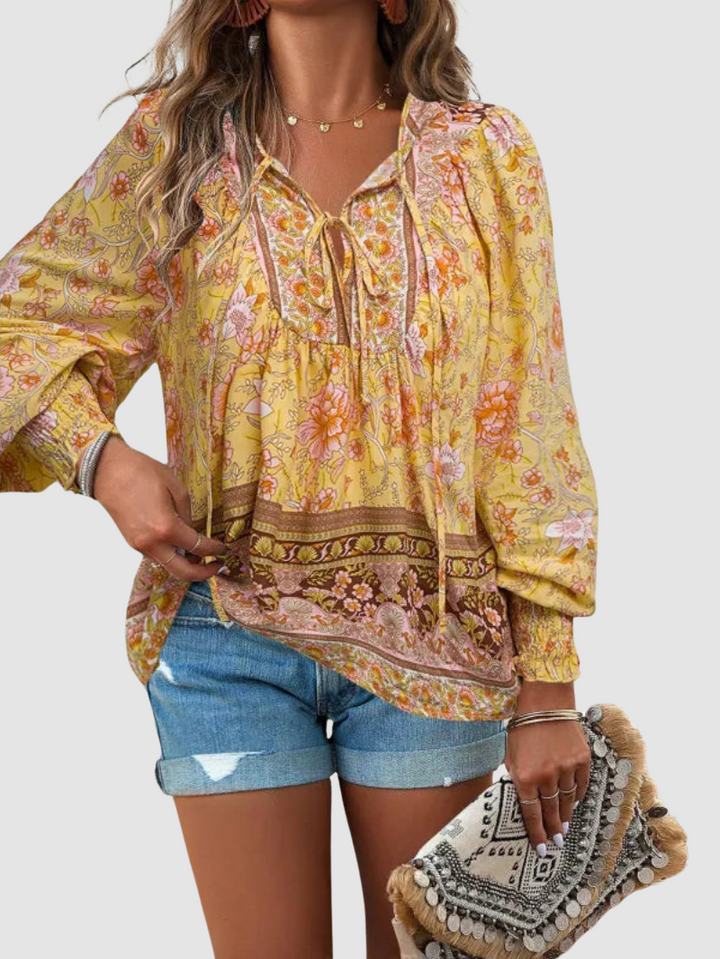 Yellow floral blouse with ornate patterns, styled with denim shorts and a decorative clutch, against a gray backdrop.