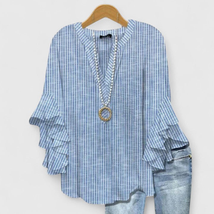 Blue striped blouse featuring ruffle sleeves, accompanied by faded jeans, displayed on wooden hanger.