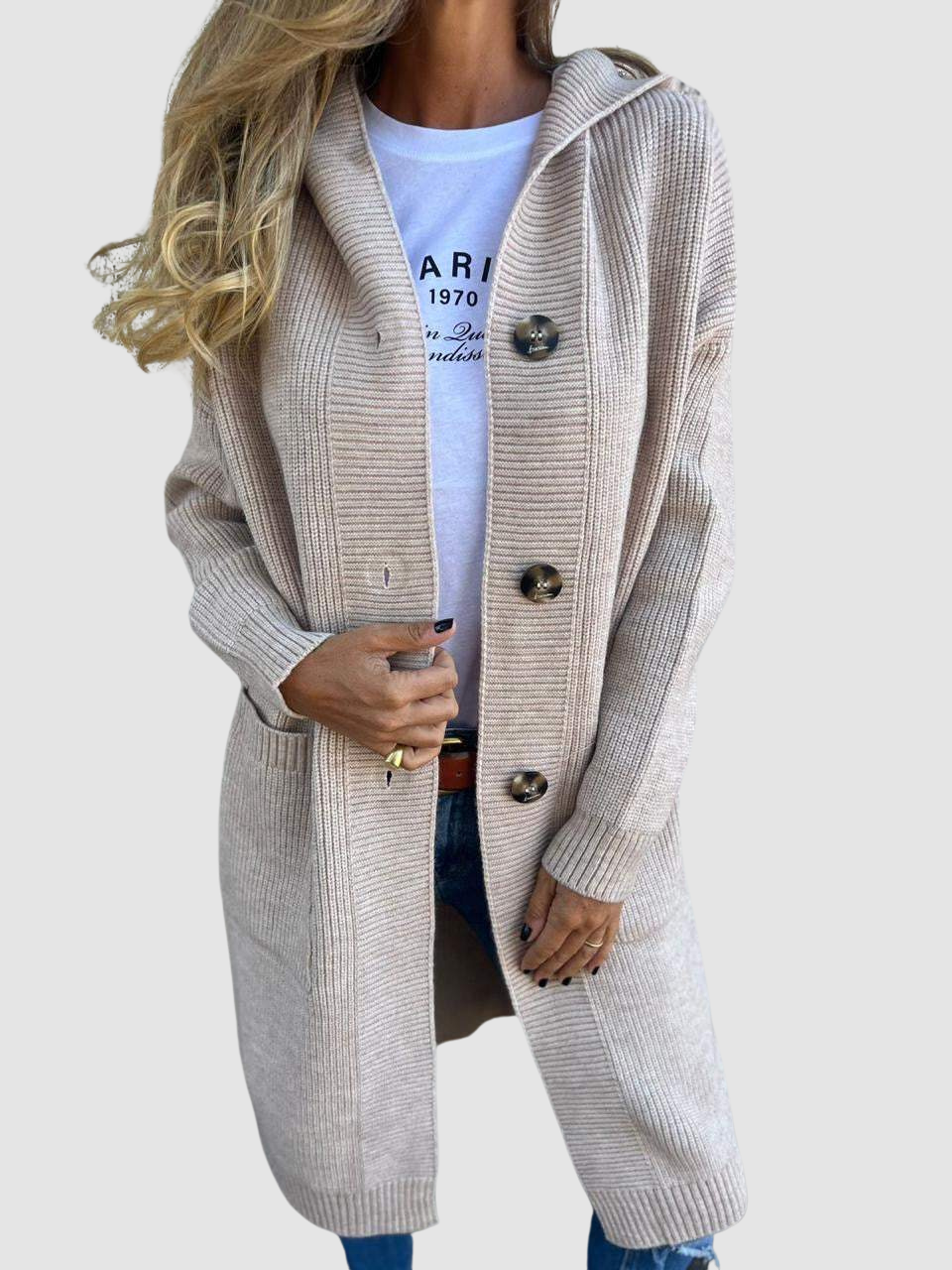 Beige knitted cardigan with large buttons and pockets, worn over a white graphic tee and jeans in studio setting.