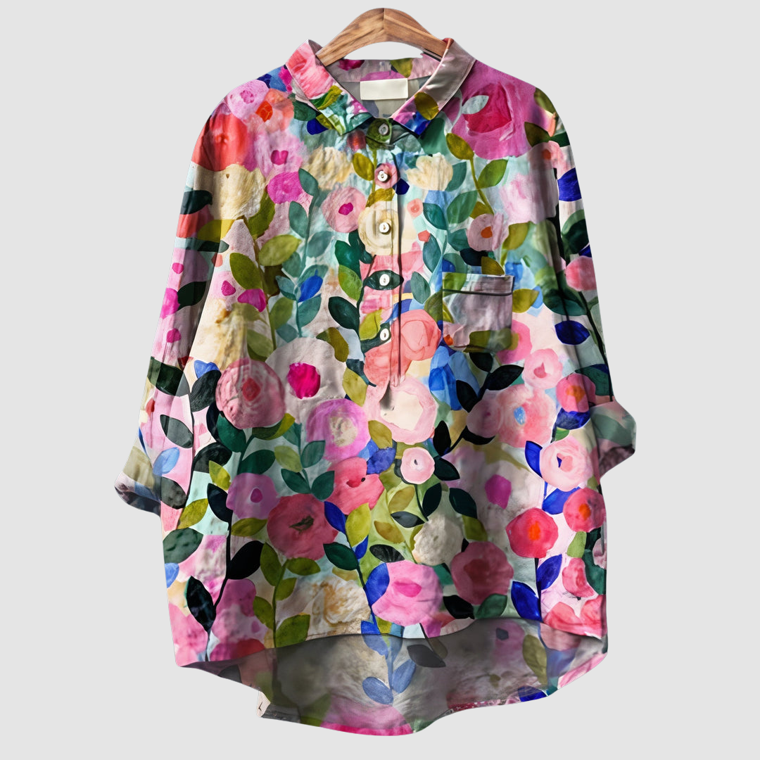 Vibrant floral print blouse with button front and pocket on wooden hanger against light gray background.