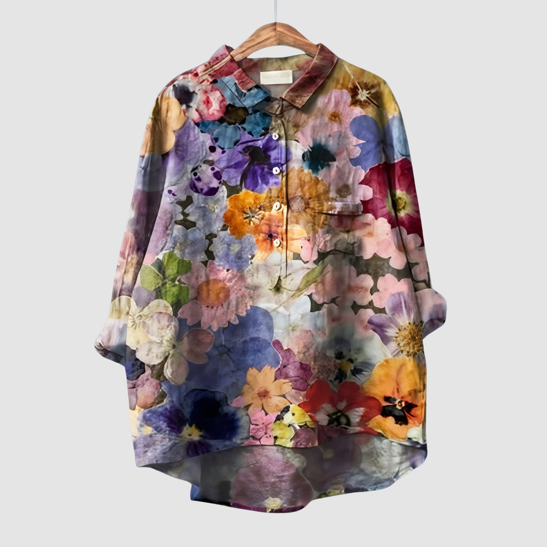 Multicolored floral print blouse on wooden hanger with button front against light gray background.