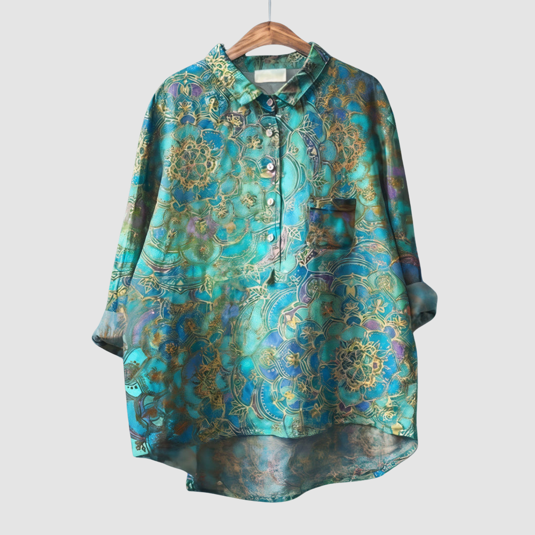 Blue and gold patterned blouse with intricate details on wooden hanger against light gray background.