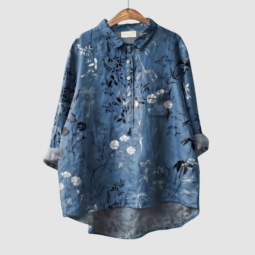 Blue blouse with white floral and foliage print on wooden hanger against light gray background.