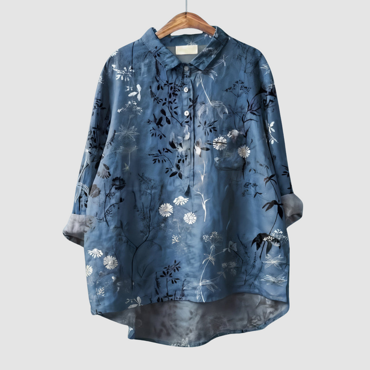 Blue blouse with white floral and foliage print on wooden hanger against light gray background.