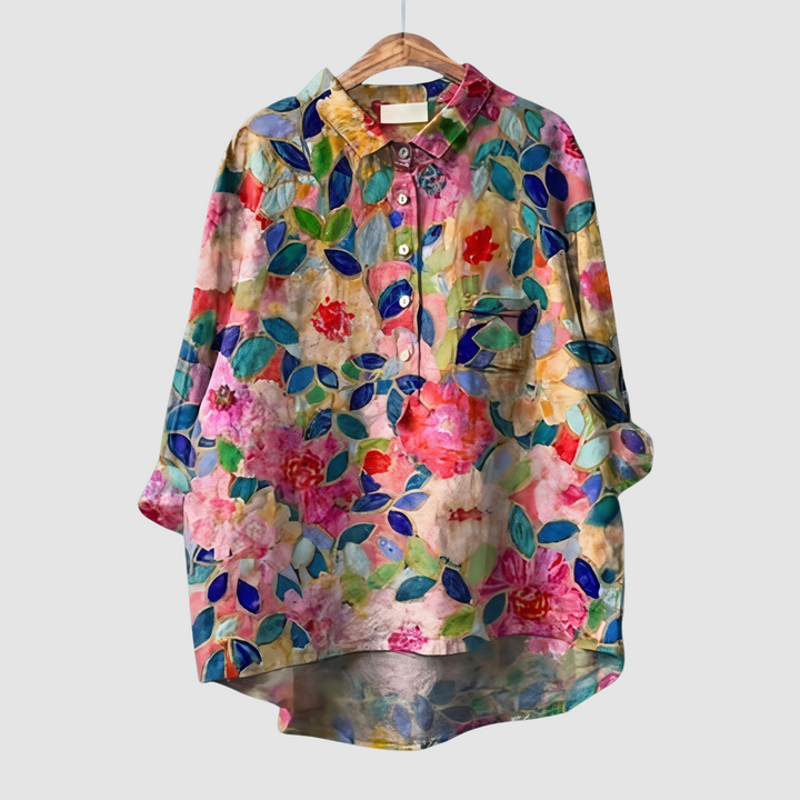 Lush colorful floral blouse with vivid patterns on wooden hanger against light gray background.