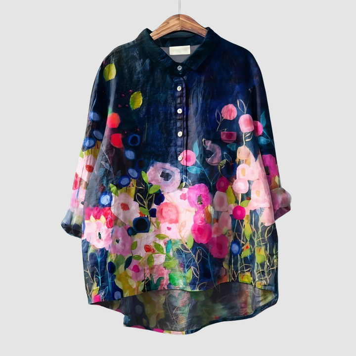 Bright floral blouse with a dark background and vibrant flowers on wooden hanger against light gray background.