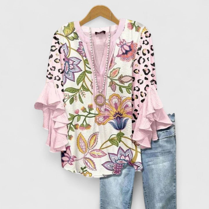 Colorful floral blouse with pink ruffle sleeves and leopard print, accompanied by light jeans, on wooden hanger.