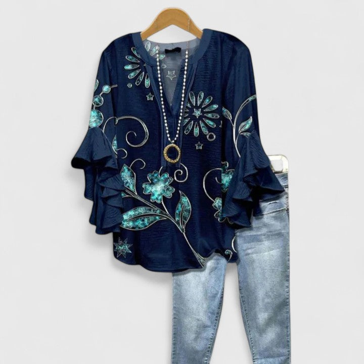 Navy blouse with teal floral embellishments and ruffle sleeves, paired with light jeans, on wooden hanger.
