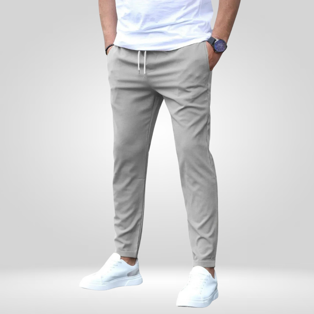 Gray stretch pants with drawstring, modeled with white t-shirt and sneakers in a studio with gray backdrop.