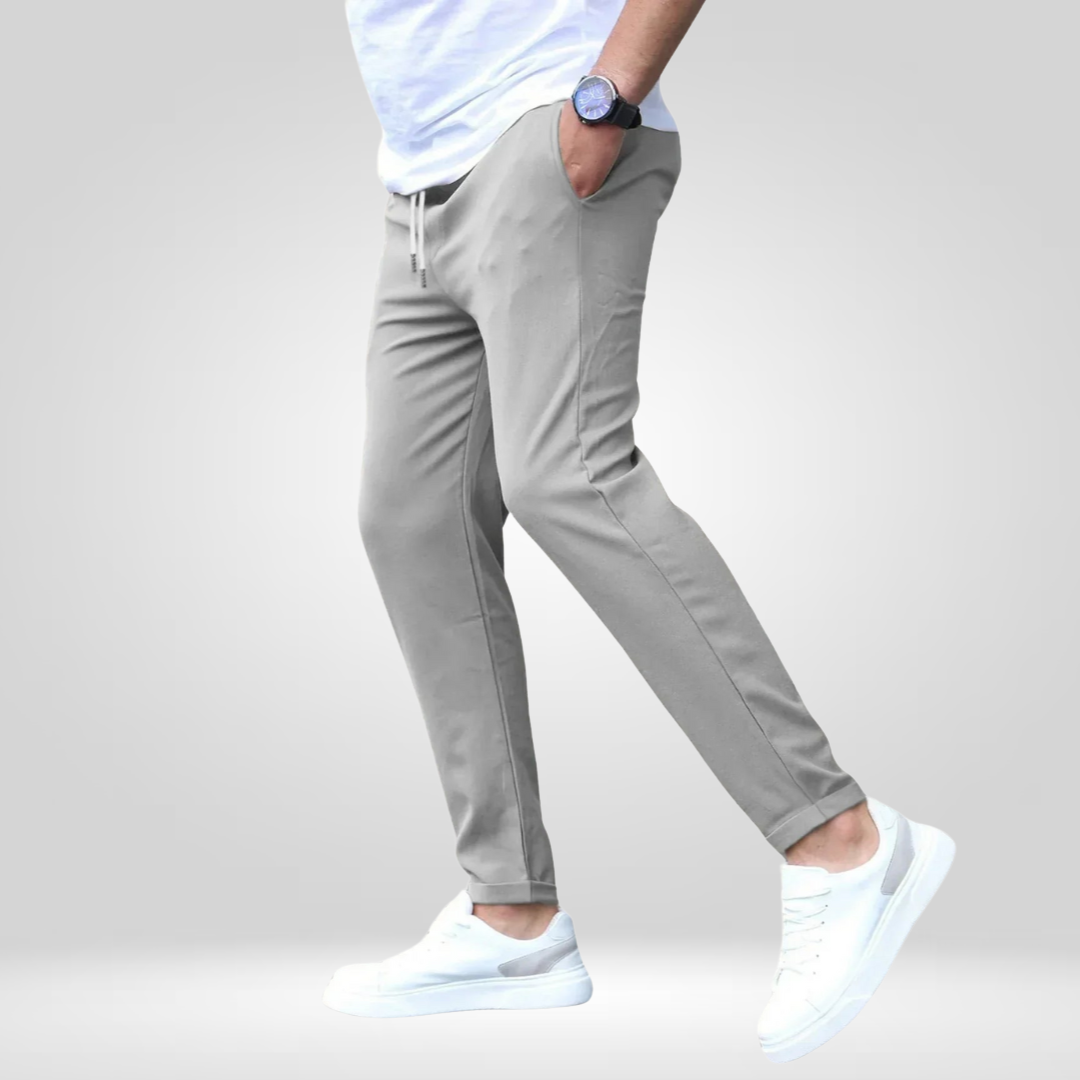 Side view of gray stretch pants with white t-shirt and sneakers, modeled in a studio with gray background.