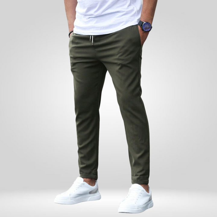 Olive stretch pants with drawstring, modeled with white t-shirt and white sneakers in a studio setting.