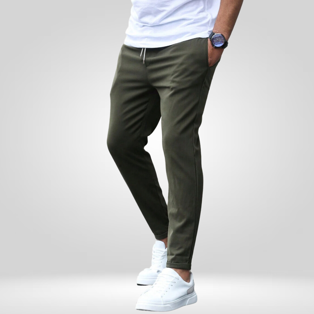 Model wearing olive stretch pants, white t-shirt, sneakers against a gray studio backdrop.