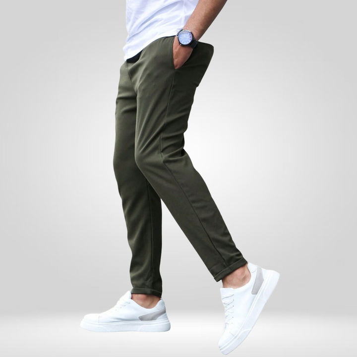 Side profile of olive stretch pants with white sneakers and t-shirt, modeled in a gray studio.