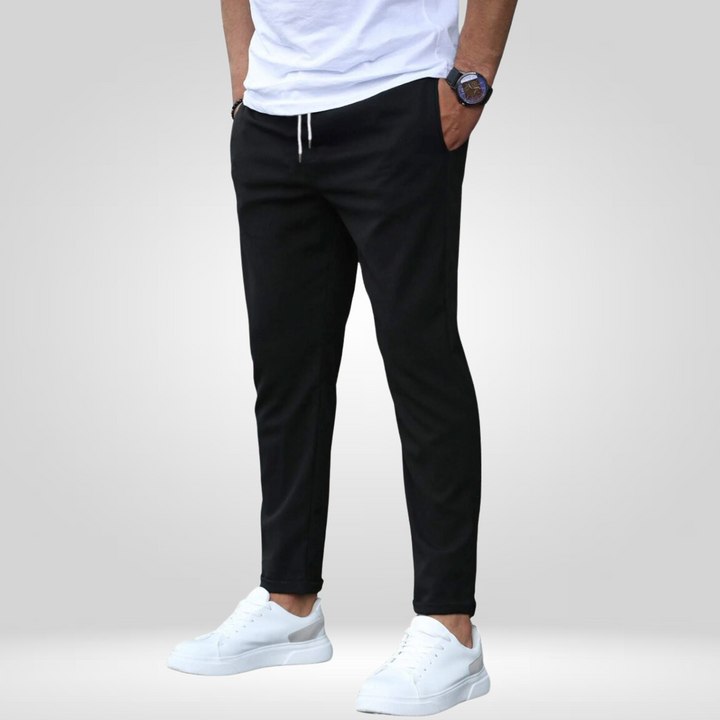 Black stretch pants with white t-shirt and white sneakers, modeled in a studio with gray background.