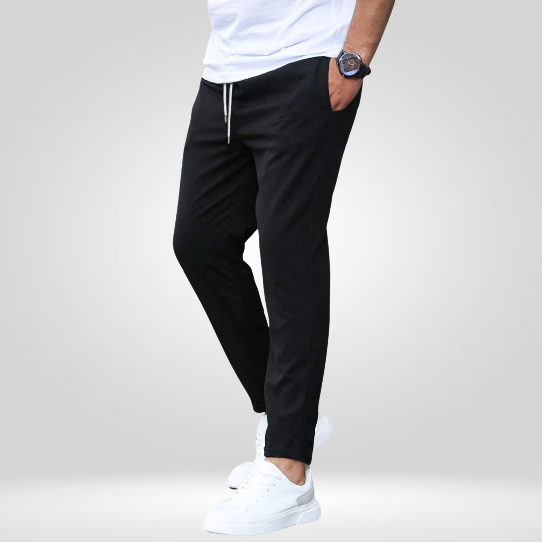 Model wearing black stretch pants, white sneakers, and t-shirt in a studio with gray backdrop.