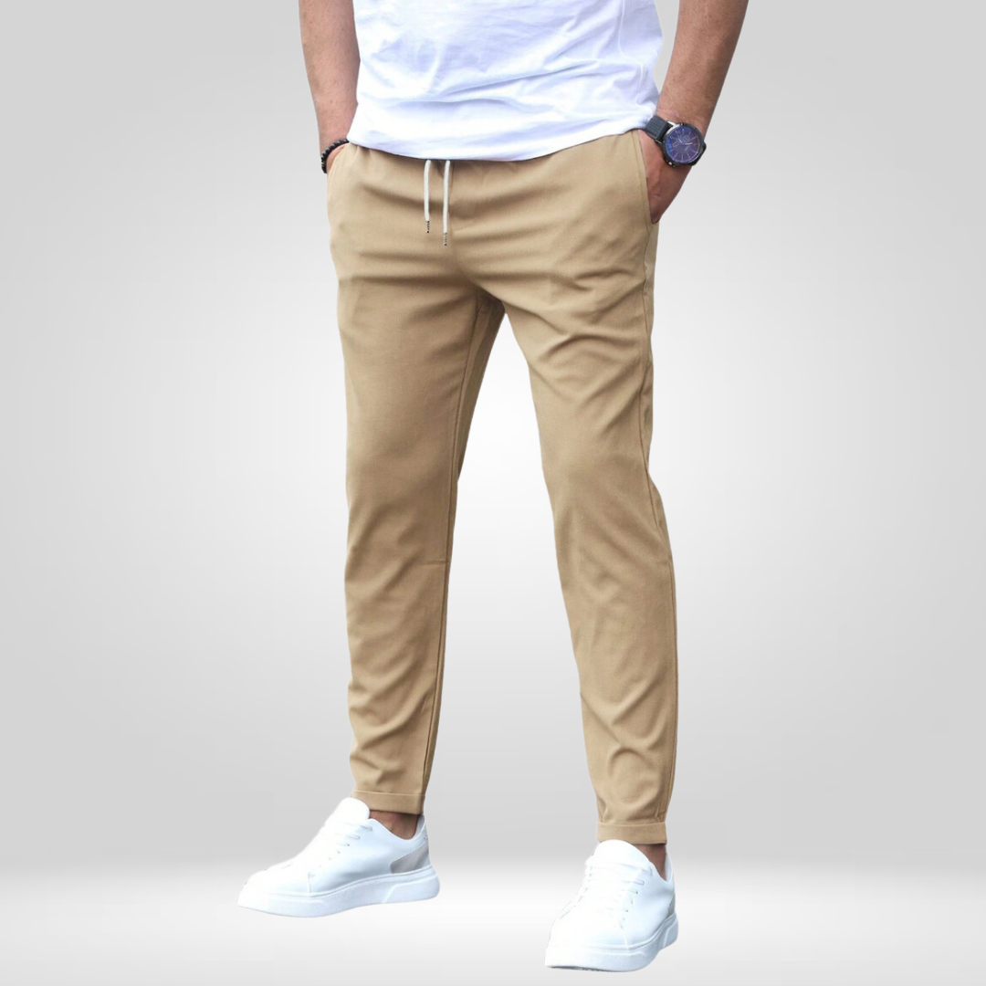Tan stretch pants with drawstring, modeled with white t-shirt and sneakers on a gray studio backdrop.