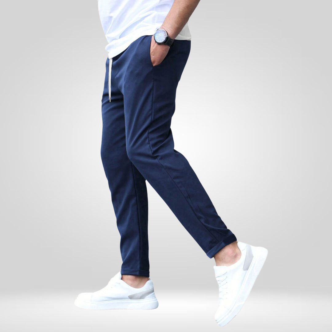 Side view of navy stretch pants with white sneakers and t-shirt, modeled in a gray studio.