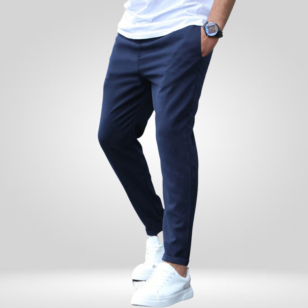Model wearing navy stretch pants, white t-shirt, and sneakers in a studio with gray backdrop.