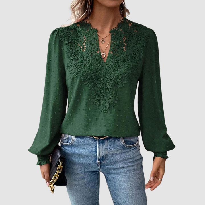 Green V-neck lace blouse with intricate design, long sleeves, paired with blue jeans, model holding a black purse, gray background.