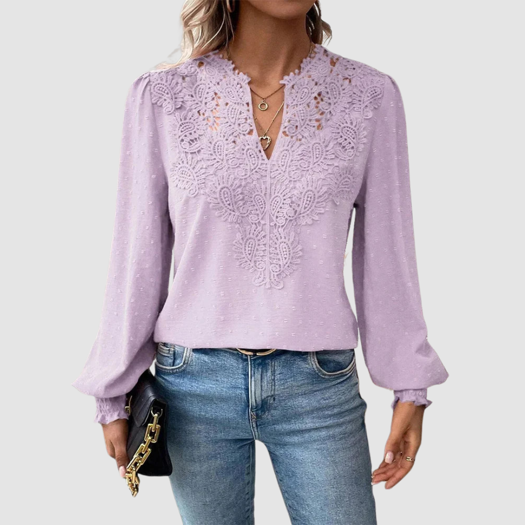 Lilac V-neck lace blouse with intricate design, long sleeves, paired with blue jeans, model holding a black purse, gray background.