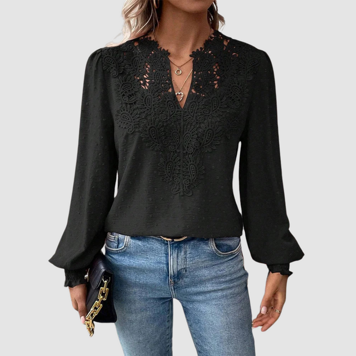 Black V-neck lace blouse with intricate design, long sleeves, paired with blue jeans, model holding a black purse, gray background.