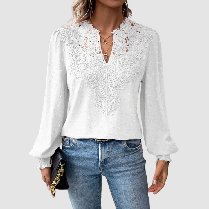 White V-neck lace blouse with intricate design, long sleeves, paired with blue jeans, model holding a black purse, gray background.
