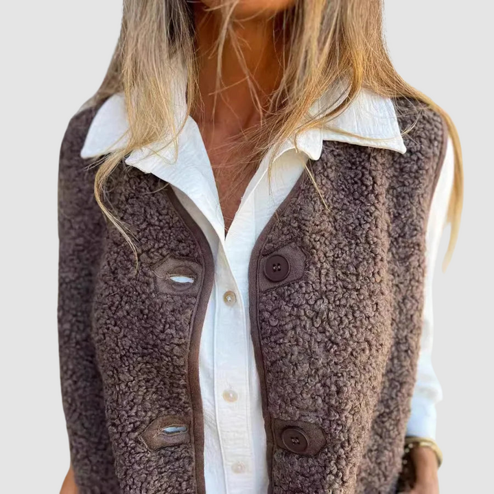 Close-up of a brown buttoned vest with textured finish worn over a white shirt in a studio setting.