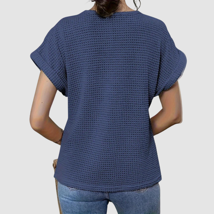 Back view of woman in a navy textured top paired with jeans, studio background.